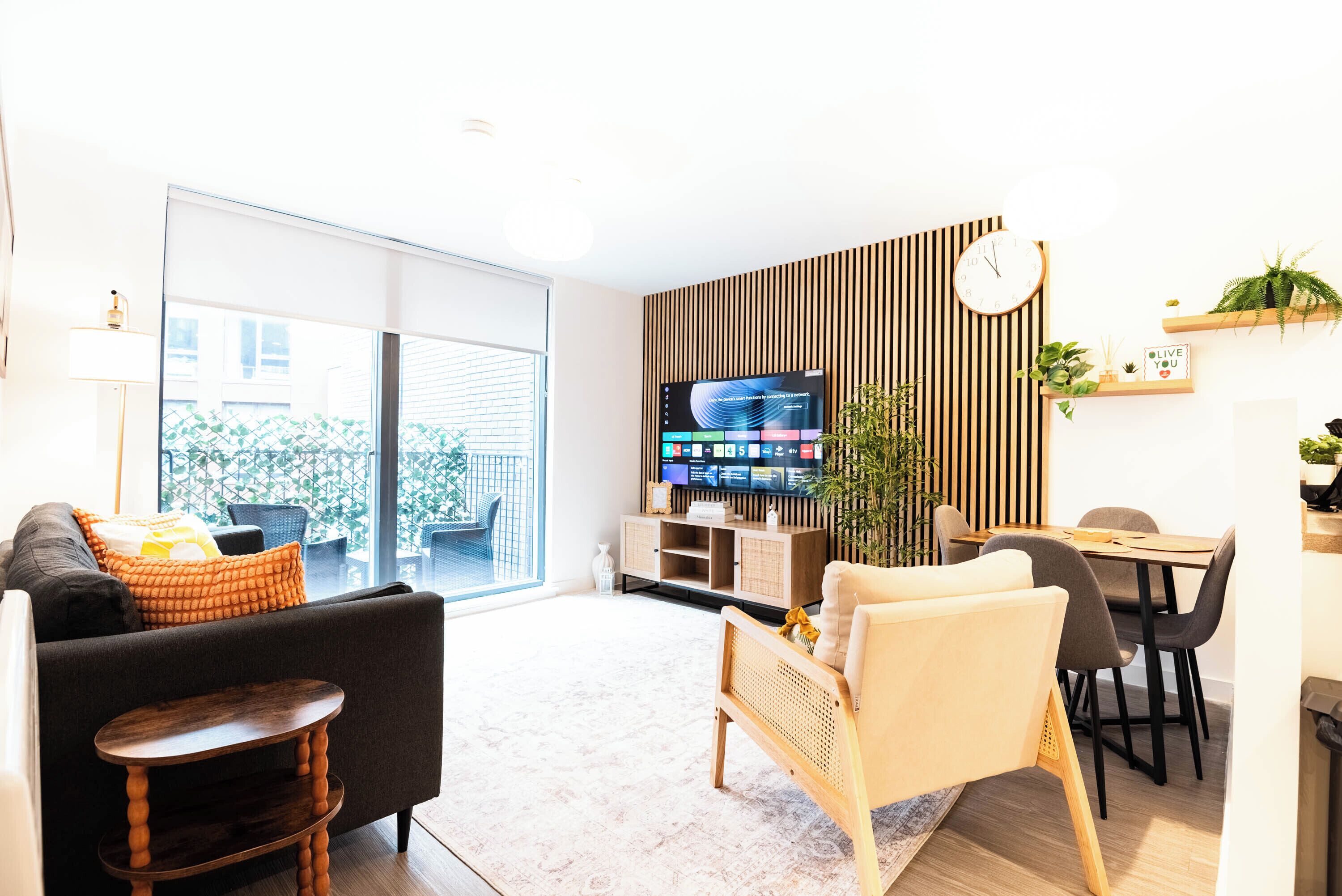 A modern living room with a sofa, a coffee table, a TV, and a dining area with chairs and a table.