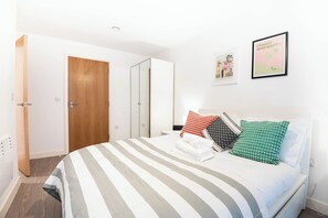 Quarto de hotel com cama, porta de madeira, parede branca e quadro emoldurado.