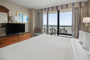 Een hotelkamer met een groot bed, een televisie, een dressoir, een stoel en uitzicht op zee.