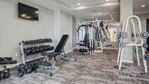 Een sportschool met gewichthefapparatuur, dumbbells en een televisie aan de muur.