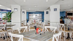Een restaurant met witte stoelen en tafels, een bar en een wand vol wijnflessen.