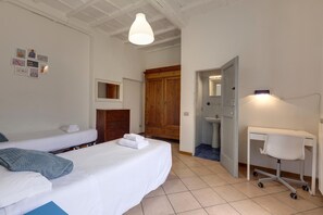A bedroom with two beds, a desk with a chair, a wooden wardrobe, and a bathroom visible through an open door. - Ginori 3 G in Firenze (Florence)