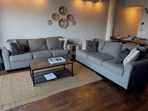 Ein modernes Wohnzimmer mit grauen Sofas, einem Couchtisch und einem Essbereich mit Holztisch und Stühlen.