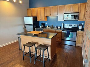 A modern kitchen with wooden cabinets, a stainless steel refrigerator, a microwave, an oven, and a bar area with stools. - Spacious two bedroom with pool (Sandusky)