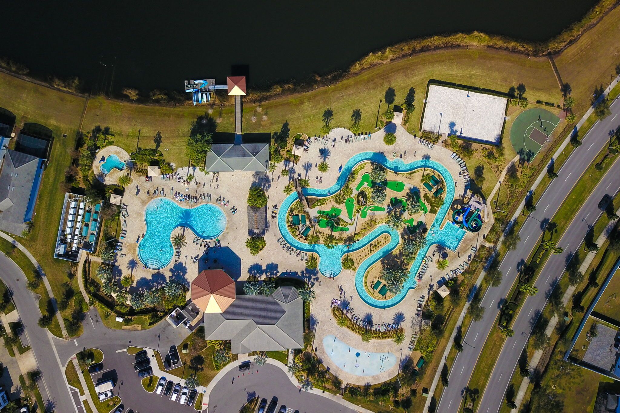 An aerial view of a resort with multiple swimming pools, a basketball court, and a large parking area.