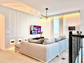 A modern living room with a grey sofa, a flat-screen TV mounted on the wall, and a ceiling light fixture. - Spacious and Modern Retreat w/ Pool & Spa, Walk to Clubhouse (Kissimmee)