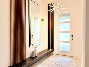 A modern interior with a large mirror, a wall-mounted light fixture, and a door with frosted glass panels. - Spacious and Modern Retreat w/ Pool & Spa, Walk to Clubhouse (Kissimmee)