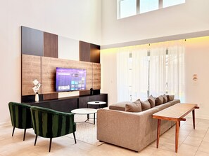 Ein modernes Wohnzimmer mit Flachbildfernseher an einer Holzpaneelwand, einer Couch, einem Couchtisch und einem Esstisch.