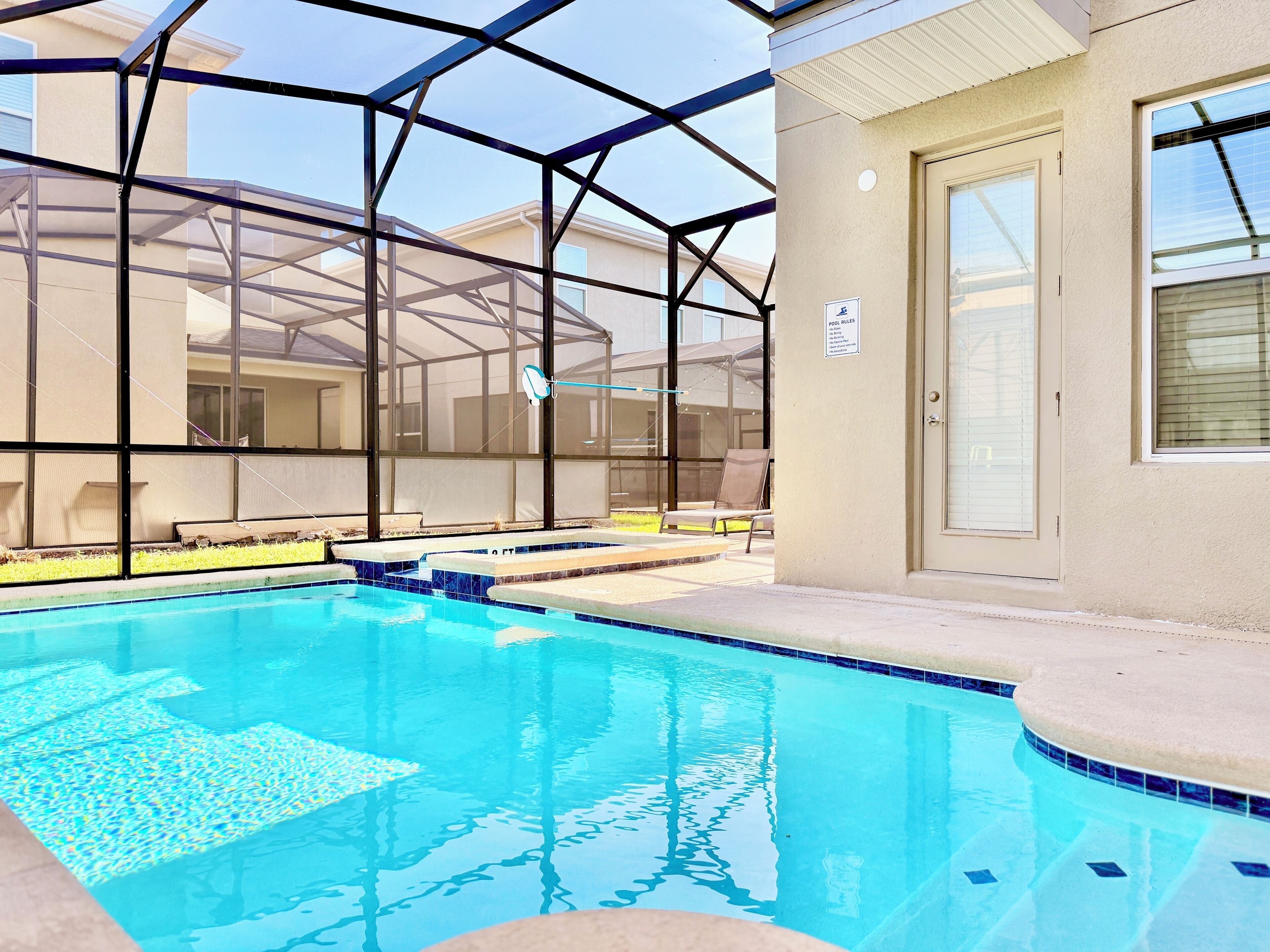An indoor swimming pool with a glass enclosure, a poolside chair, and a door with a pool rules sign.