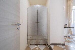 Una habitación con armario, una puerta, una ventana con cortinas y suelo de baldosas.