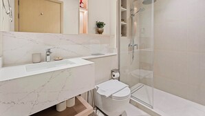Ein modernes Badezimmer mit Marmorplatte, einer Duschkabine aus Glas und einem Holzschrank.