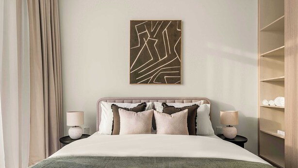 Ein Hotelzimmer mit einem Bett, zwei Nachttischen, einem an der Wand befestigten abstrakten Kunstwerk, einem Kleiderschrank und einem großen Fenster mit Vorhängen.