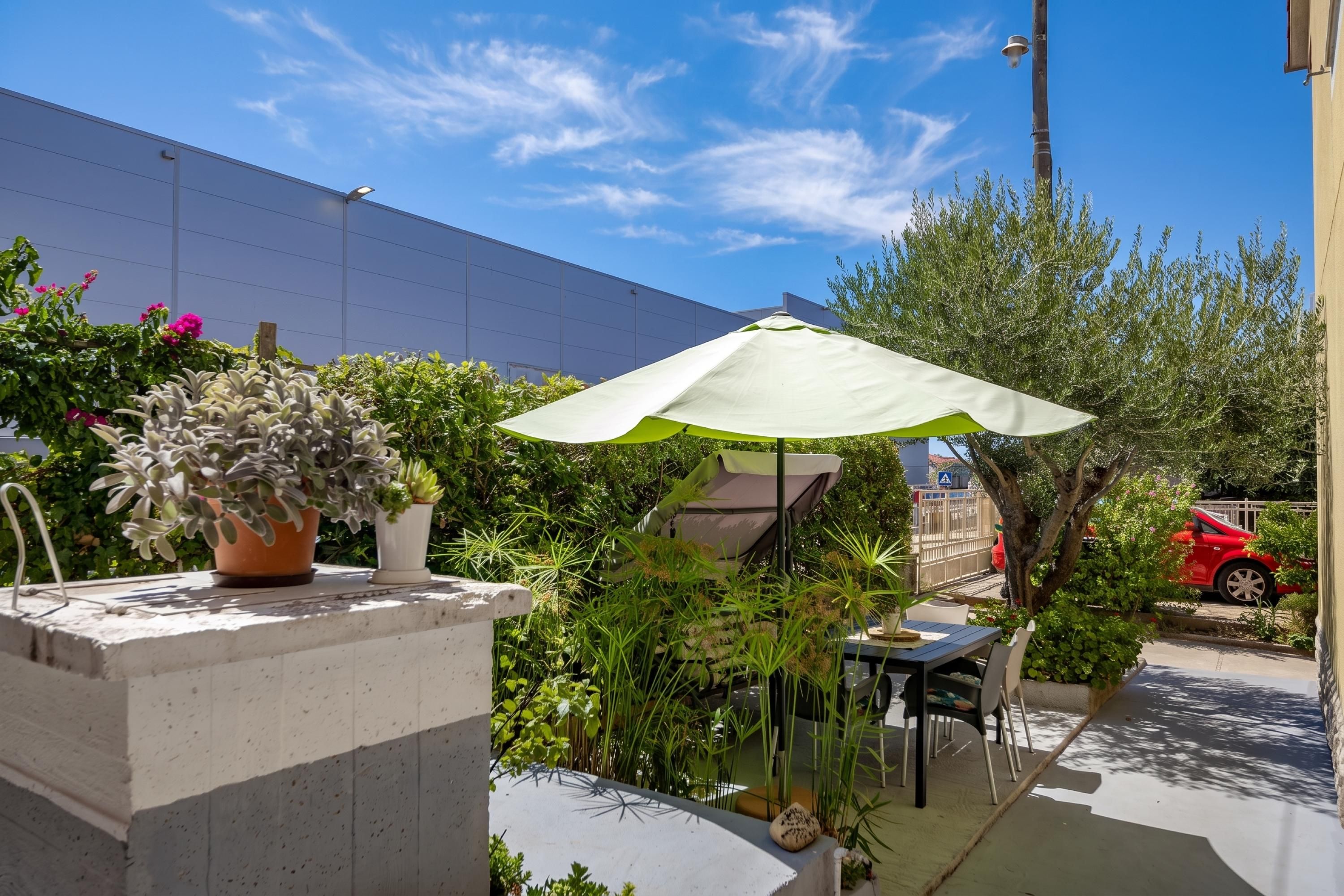 An outdoor patio with a table and chairs, surrounded by potted plants and a large umbrella.