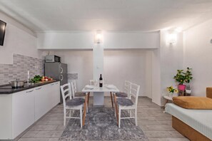 A compact kitchen with a dining area, a refrigerator, a microwave, and a dining table set with plates, wine glasses, and a bottle. - Klarić Residence (Zadar)