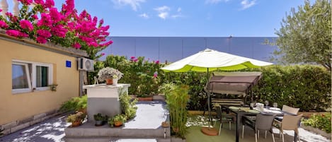Un patio con mesa y sillas, rodeado de plantas en macetas y una pared blanca.