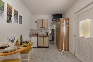 A compact kitchen with a dining area, a wooden cabinet, and a white door. - Klarić Residence (Zadar)