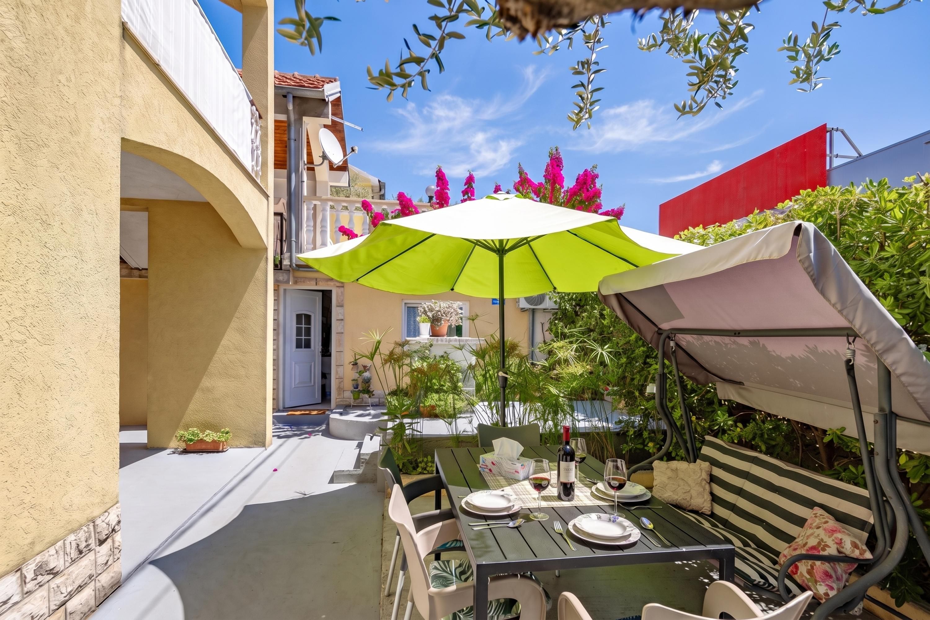 An outdoor dining area with a table set for two, a green umbrella, and a red awning.