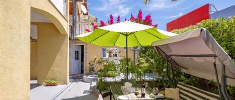 An outdoor dining area with a table set for two, a green umbrella, and a red awning.