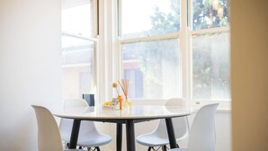 A round table with four chairs, a vase with a candle, and a small box, all in a bright room with large windows. - Metawise 2BR Apt Brightest in Brighton (Sydney)