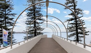 A pedestrian bridge with metal arches, a concrete walkway, and a view of a body of water and trees. - Metawise 2BR Apt Brightest in Brighton (Sydney)