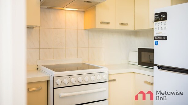 A kitchen with a white stove, oven, and microwave, a white refrigerator, and light-colored cabinets. - Metawise 2BR Apt Brightest in Brighton (Sydney)
