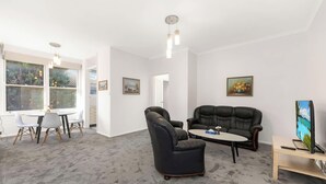 A modern living room with a black leather sofa, a dining table with chairs, and artwork on the walls. - Metawise 2BR Apt Brightest in Brighton (Sydney)