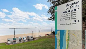 Un letrero en la playa con indicaciones hacia Brighton Le Sands y atracciones cercanas.