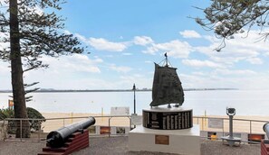 A coastal monument with a cannon, a plaque, and a telescope, overlooking a beach and water. - Metawise 2BR Apt Brightest in Brighton (Sydney)
