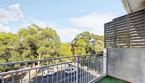 A balcony with a view of a street, trees, and a building in the background. - Metawise 2BR Apt Brightest in Brighton (Sydney)