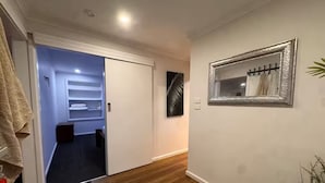 A hallway with a wooden floor, a white door, a mirror on the wall, and a plant. - Gates Mini Ranch (Waterloo Corner)