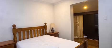 A bedroom with a wooden bed, a ceiling fan, a nightstand, and a window with curtains.