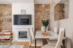 A modern dining area with a fireplace, a flat-screen TV mounted above it, and a dining table set with chairs. - Modern 3-bedroom Home Near Westfield Central Lond (London)
