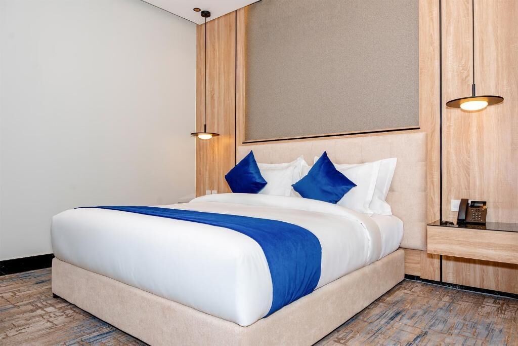 Ett hotellrum med en säng, ett nattduksbord med en telefon och en väggmonterad lampa.