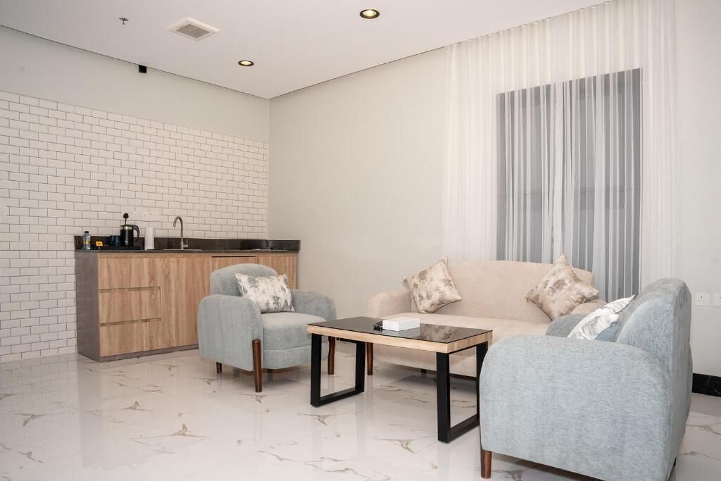 Una sala de estar moderna con un sofá, sillones, una mesita de centro y una cocina con encimera y lavamanos.