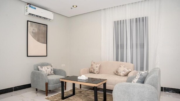 Un salon moderne comprenant un canapé, deux fauteuils, une table basse et un appareil de climatisation fixé au mur.