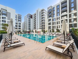 Ein Dachpool mit Liegestühlen und Sonnenschirmen, umgeben von Hochhäusern.