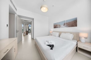 Ein modernes Hotelzimmer mit einem großen Bett, Nachttischlampen, Blick ins Freie und einer Tür zu einem weiteren Raum.