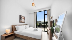 Ein modernes Schlafzimmer mit einem großen Bett, einem Nachttisch mit Lampe, einem Gemälde an der Wand und Blick ins Freie durch ein großes Fenster.