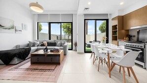 Ein modernes Wohnzimmer mit einem grauen Sofa, einem Couchtisch und einem Essbereich mit weißen Stühlen und einem Tisch.