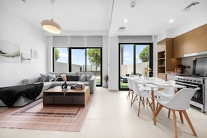 Ein modernes Wohnzimmer mit einem grauen Sofa, einem Couchtisch und einem Essbereich mit weißen Stühlen und einem Tisch.