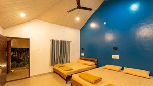 Ein Zimmer mit zwei Betten, einem Deckenventilator und Blick auf einen tropischen Garten.