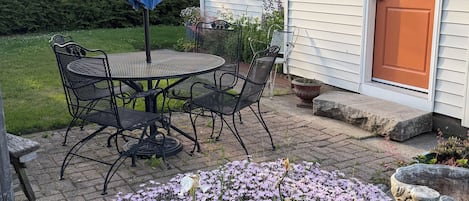A patio with a table and chairs, a blue umbrella, and a garden with flowers.