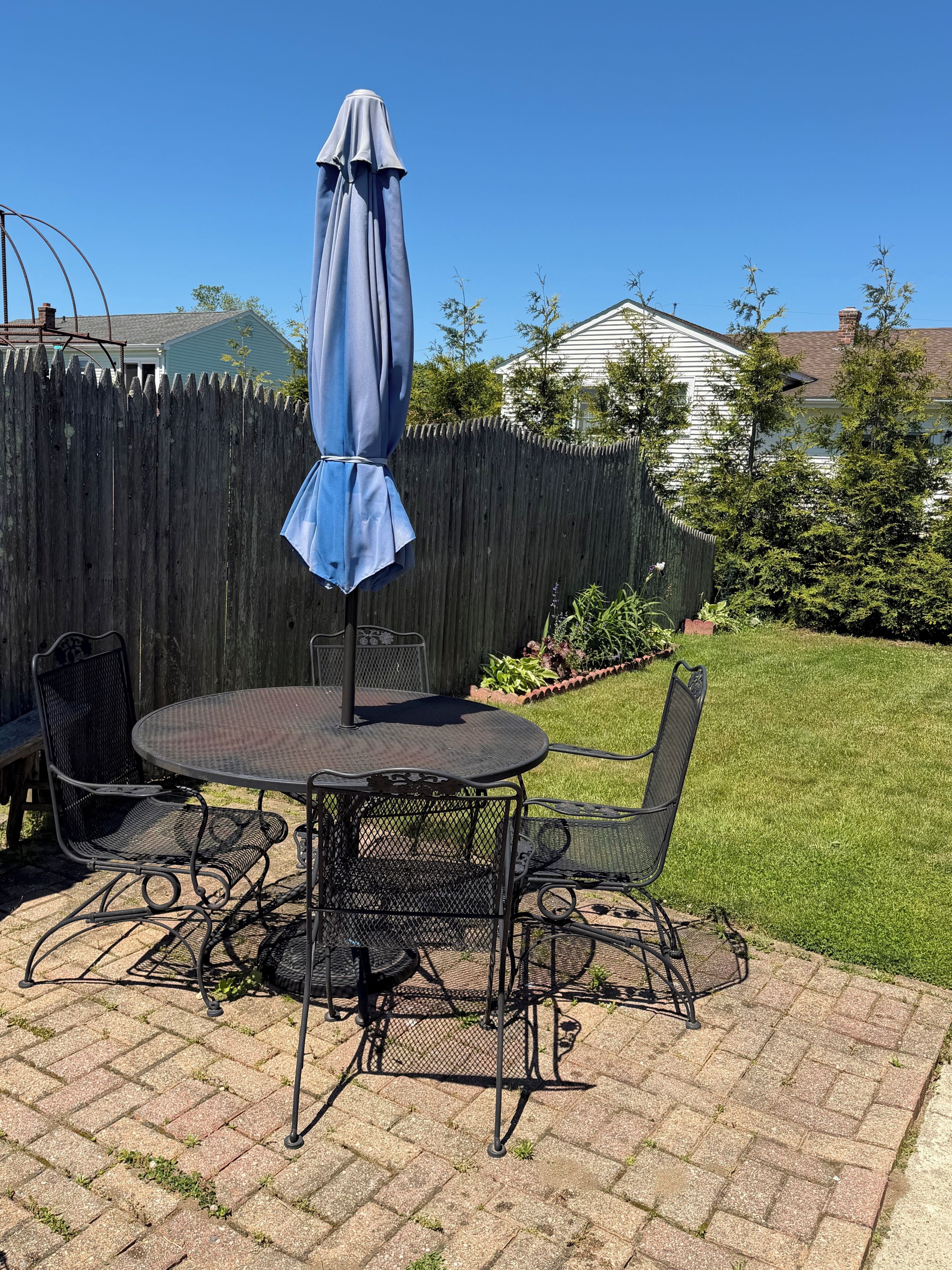 A patio with a round table and chairs, a blue umbrella, and a wooden fence in the background.
