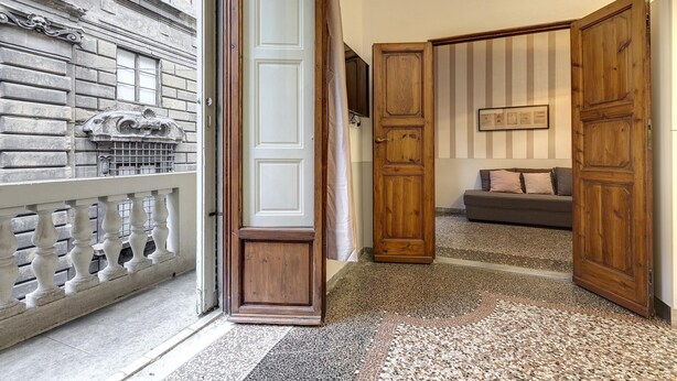 A hallway with a stone wall, a wooden door, and a grey sofa. - Proconsolo 9S in Firenze (Florence)