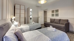 A hotel room with two beds, a sofa, a desk with a lamp, and a hanging light fixture. - Proconsolo 9S in Firenze (Florence)