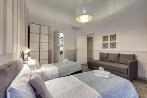 A hotel room with two beds, a sofa, a desk with a lamp, and a hanging light fixture. - Proconsolo 9S in Firenze (Florence)