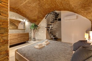 Ein Schlafzimmer mit Ziegeldecke, einem Bett mit gemustertem Überwurf, einer hölzernen Kommode, einem Spiegel und einer Treppe.