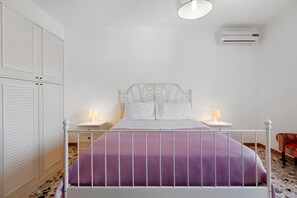 Ein Schlafzimmer mit einem Bett, zwei Nachttischen mit Lampen, einem Kleiderschrank und einer Klimaanlage.