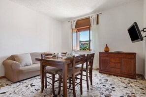 Ein Essbereich mit Holztisch und -stühlen, einer Couch, einem Holzschrank und einem an der Wand befestigten Fernseher.