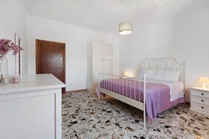 Ein Schlafzimmer mit Bett, Nachttischen, einem Kleiderschrank, einem Schreibtisch und einer Pendelleuchte.